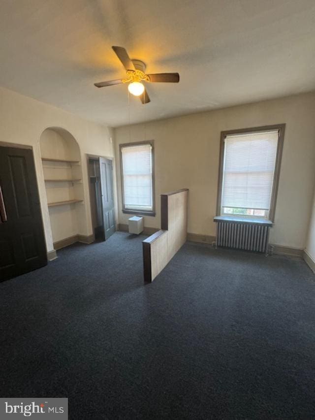 spare room featuring radiator heating unit, dark carpet, ceiling fan, and built in shelves