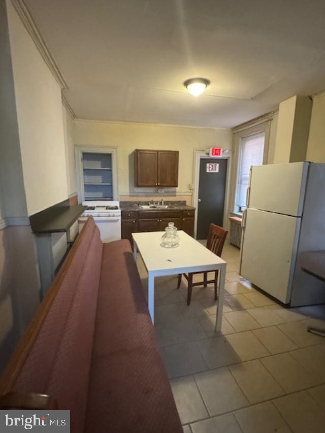 kitchen with dark brown cabinets, white appliances, sink, and light tile patterned floors