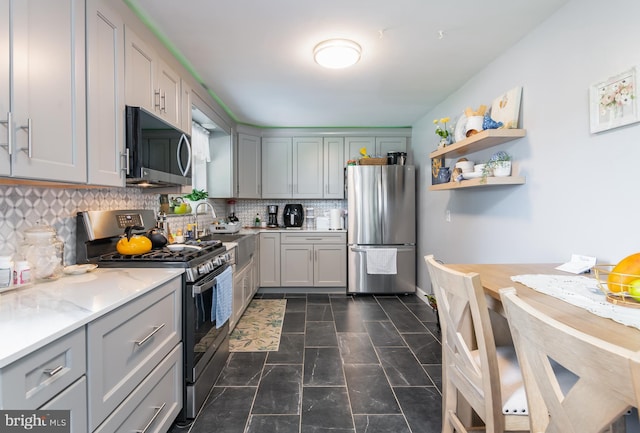 kitchen with decorative backsplash, gray cabinets, light stone counters, and appliances with stainless steel finishes