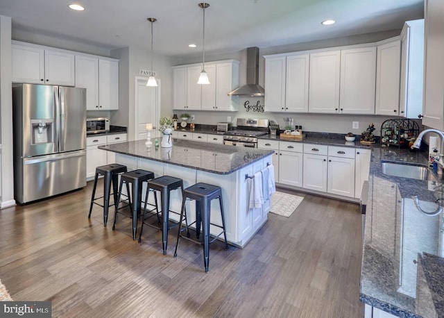 kitchen with wall chimney exhaust hood, stainless steel appliances, sink, hardwood / wood-style flooring, and white cabinets