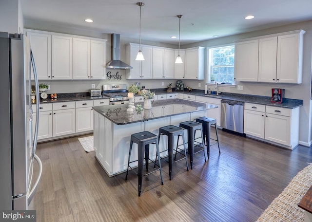 kitchen with a center island, white cabinets, wall chimney range hood, and appliances with stainless steel finishes