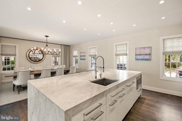 kitchen featuring pendant lighting, dark wood-type flooring, a center island with sink, sink, and white cabinetry