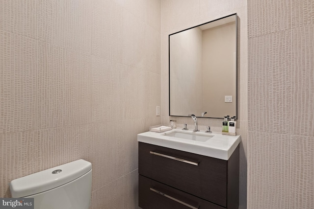 bathroom featuring vanity, toilet, and tile walls