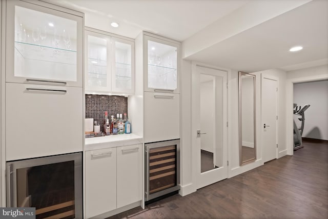 bar with tasteful backsplash, wine cooler, white cabinets, and dark wood-type flooring