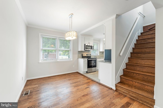 kitchen featuring crown molding, light hardwood / wood-style flooring, decorative backsplash, appliances with stainless steel finishes, and white cabinetry