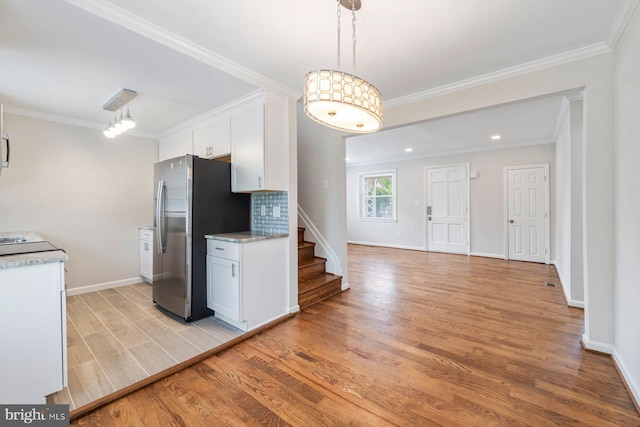 kitchen featuring backsplash, hanging light fixtures, stainless steel fridge, light hardwood / wood-style floors, and white cabinetry