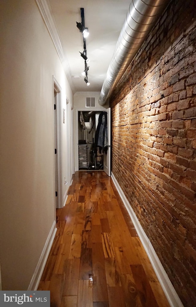 hallway with wood-type flooring, crown molding, and brick wall