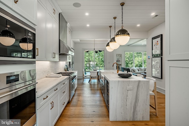 kitchen featuring a kitchen island with sink, white cabinets, stainless steel appliances, and light stone counters