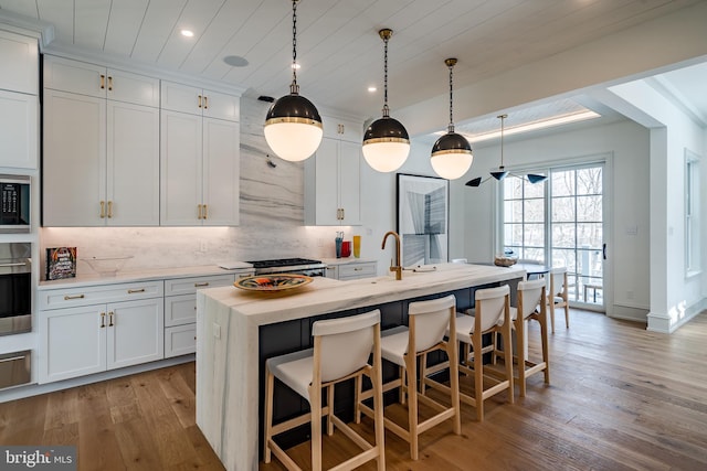 kitchen with white cabinets, decorative light fixtures, a kitchen island with sink, and light hardwood / wood-style flooring