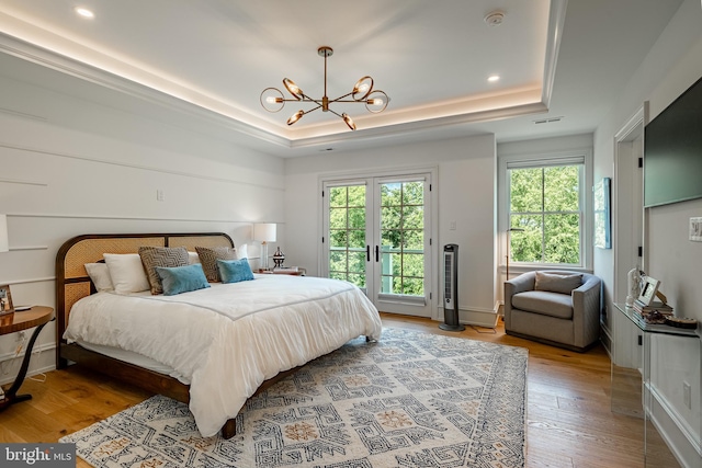 bedroom featuring hardwood / wood-style flooring, a notable chandelier, a raised ceiling, and access to exterior