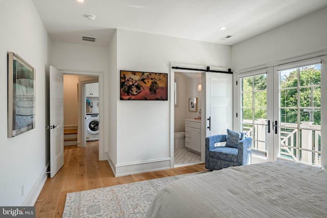 bedroom with connected bathroom, access to exterior, a barn door, washer / clothes dryer, and light hardwood / wood-style floors