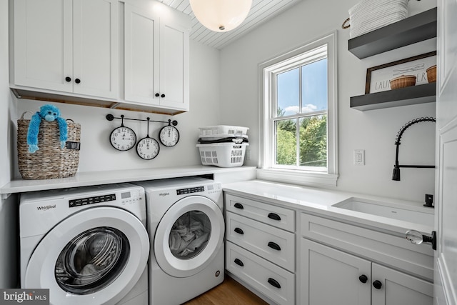 clothes washing area featuring cabinets, washing machine and dryer, hardwood / wood-style flooring, and sink