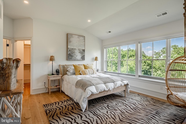 bedroom with a walk in closet, light hardwood / wood-style floors, and vaulted ceiling