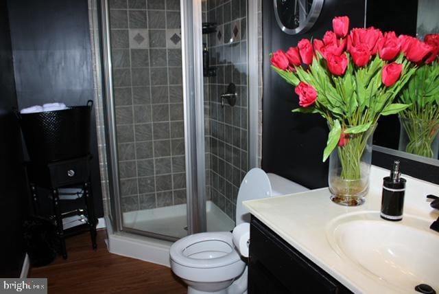 bathroom with hardwood / wood-style floors, vanity, toilet, and a shower with shower door