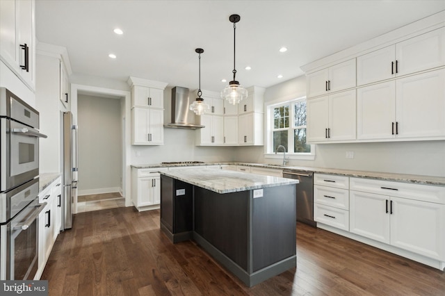 kitchen featuring a center island, wall chimney exhaust hood, stainless steel appliances, pendant lighting, and white cabinets