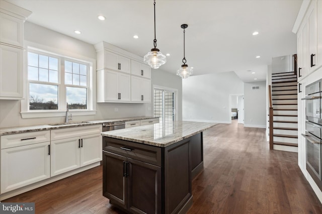 kitchen with light stone countertops, sink, decorative light fixtures, a center island, and white cabinetry