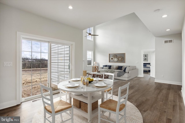 dining room with ceiling fan, a towering ceiling, and dark wood-type flooring