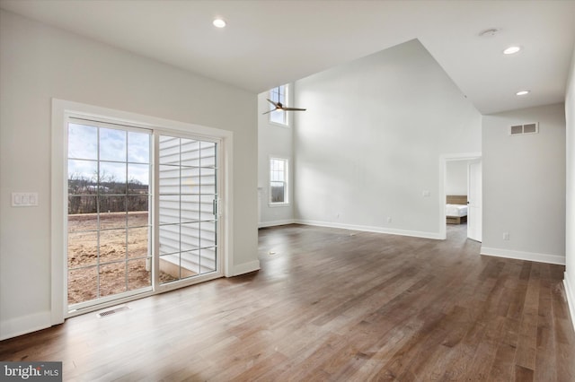 unfurnished living room with a high ceiling, dark hardwood / wood-style floors, a wealth of natural light, and ceiling fan