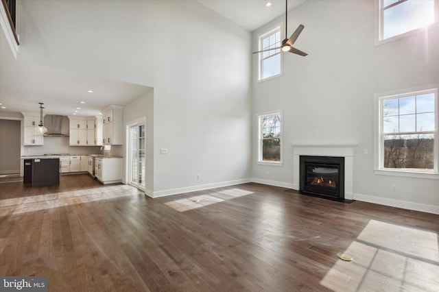 unfurnished living room with a high ceiling, ceiling fan, and dark wood-type flooring