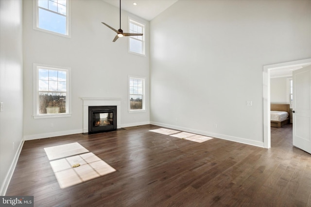 unfurnished living room featuring ceiling fan, a towering ceiling, and dark wood-type flooring