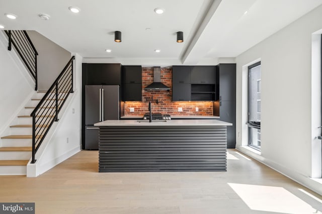 interior space featuring wall chimney exhaust hood, decorative backsplash, an island with sink, high quality fridge, and light hardwood / wood-style floors