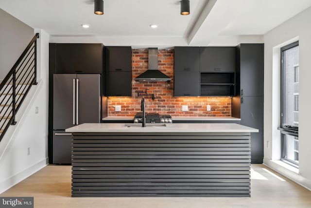 kitchen with a kitchen island with sink, high end fridge, wall chimney range hood, sink, and light hardwood / wood-style floors