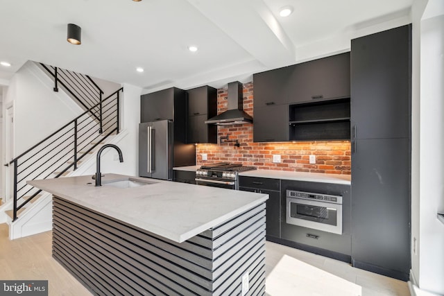 kitchen featuring sink, wall chimney range hood, premium appliances, light hardwood / wood-style flooring, and a kitchen island with sink