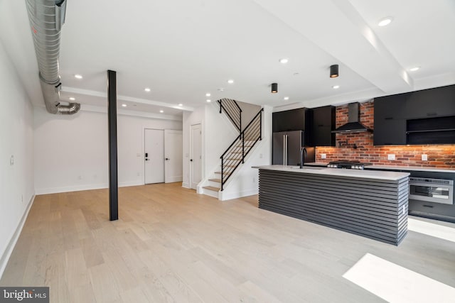 kitchen featuring light hardwood / wood-style floors, wall chimney exhaust hood, an island with sink, and appliances with stainless steel finishes