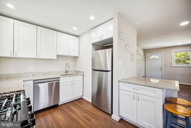 kitchen featuring stainless steel appliances, dark hardwood / wood-style flooring, sink, a breakfast bar area, and white cabinetry