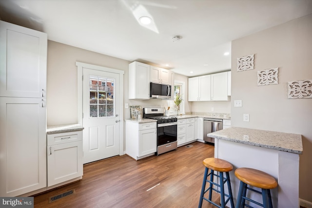 kitchen featuring stainless steel appliances, dark hardwood / wood-style flooring, light stone counters, a breakfast bar area, and white cabinetry