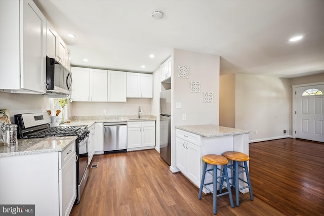 kitchen with dark hardwood / wood-style flooring, white cabinetry, appliances with stainless steel finishes, and a kitchen bar