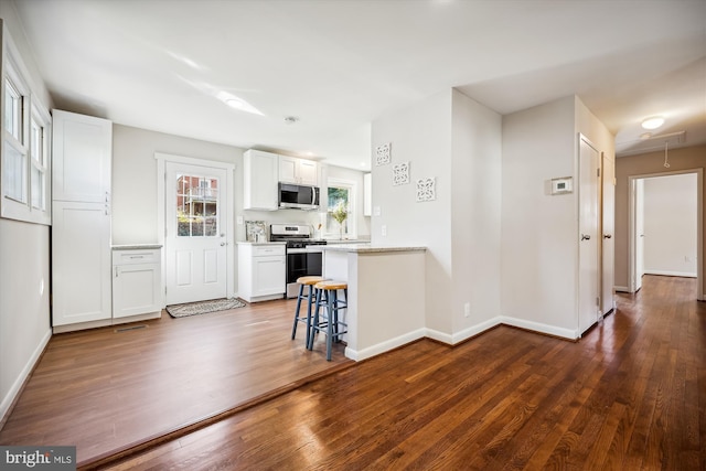 kitchen with white cabinets, appliances with stainless steel finishes, dark wood-type flooring, and a breakfast bar