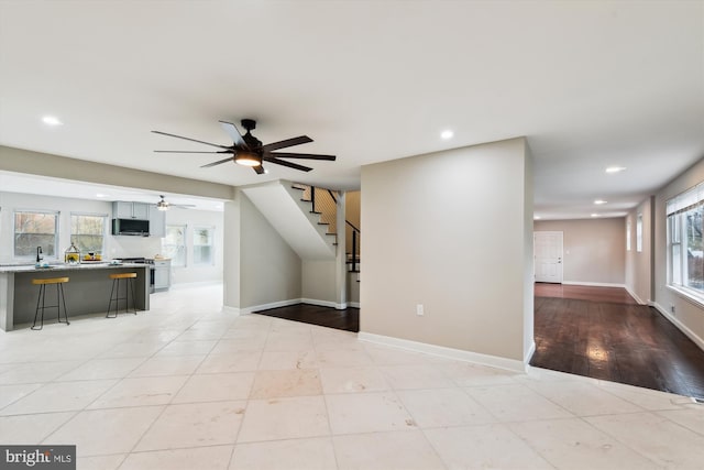unfurnished living room with a wealth of natural light, recessed lighting, a ceiling fan, and stairs