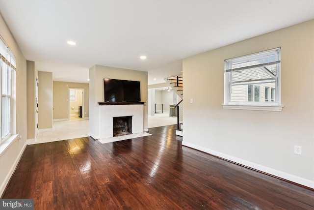 unfurnished living room featuring baseboards, recessed lighting, stairs, a fireplace with flush hearth, and hardwood / wood-style flooring