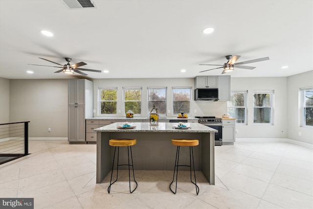 kitchen with a breakfast bar area, gray cabinets, a ceiling fan, and appliances with stainless steel finishes