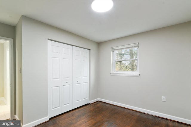 unfurnished bedroom with a closet, dark wood-style flooring, and baseboards