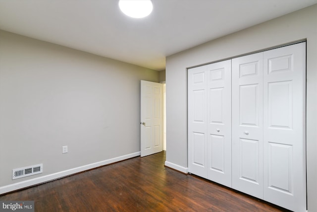 unfurnished bedroom with dark wood-type flooring, a closet, baseboards, and visible vents