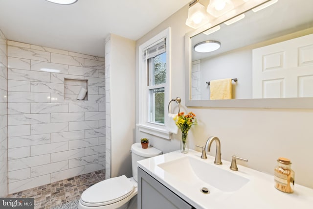 full bathroom with a tile shower, toilet, and vanity