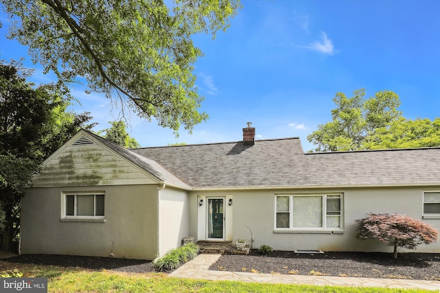 back of house with roof with shingles, a chimney, and stucco siding