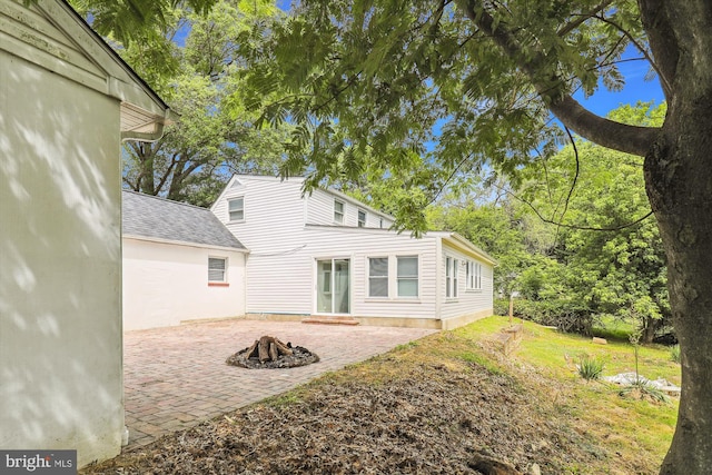 rear view of house featuring a patio area, an outdoor fire pit, a shingled roof, and a yard