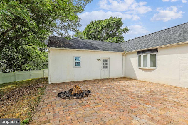 rear view of house with stucco siding, a patio, a fire pit, fence, and a shingled roof