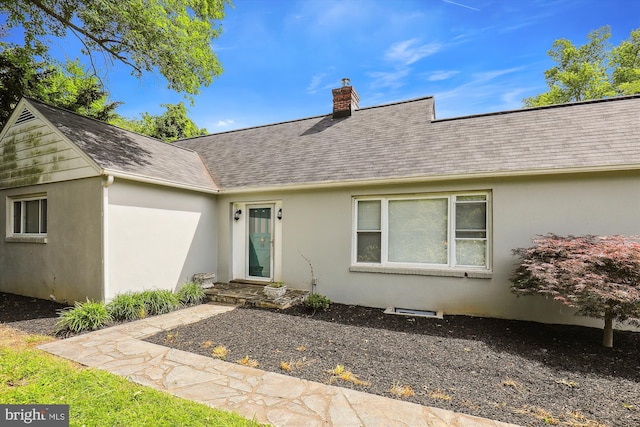 entrance to property with stucco siding, a shingled roof, and a chimney