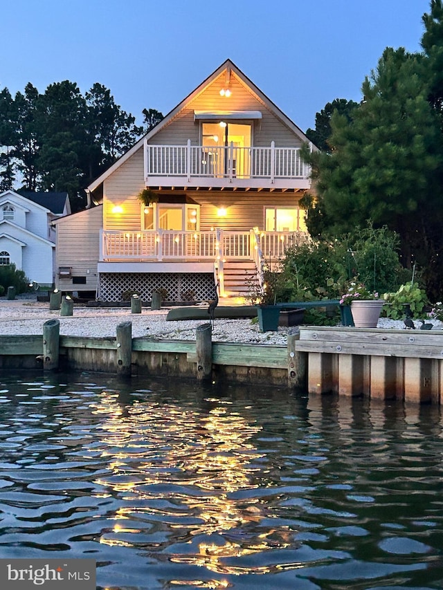 back house at dusk featuring a balcony and a deck with water view