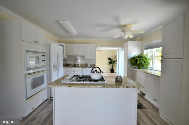 kitchen with wood-type flooring, light stone countertops, white cabinets, and white appliances