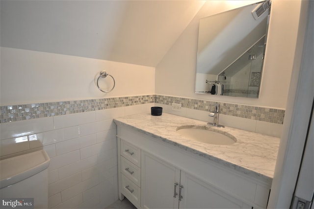 bathroom with vanity, vaulted ceiling, tile walls, and toilet