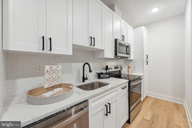 kitchen featuring appliances with stainless steel finishes, light stone counters, sink, light hardwood / wood-style flooring, and white cabinetry