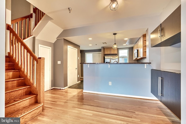 kitchen with kitchen peninsula, appliances with stainless steel finishes, decorative light fixtures, light wood-type flooring, and dark stone counters