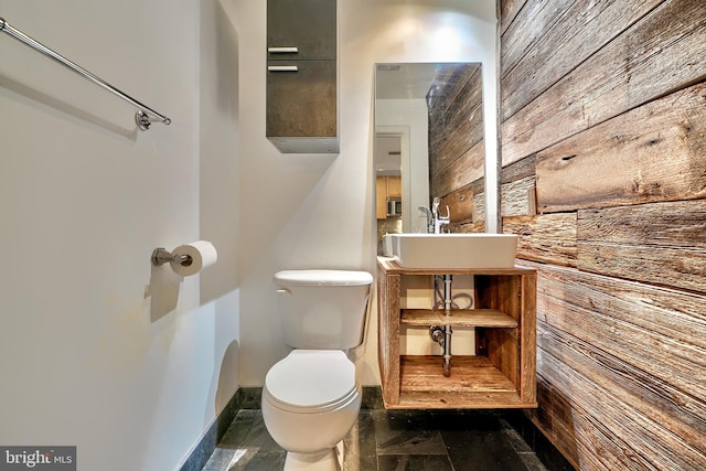 bathroom with toilet, wooden walls, and sink