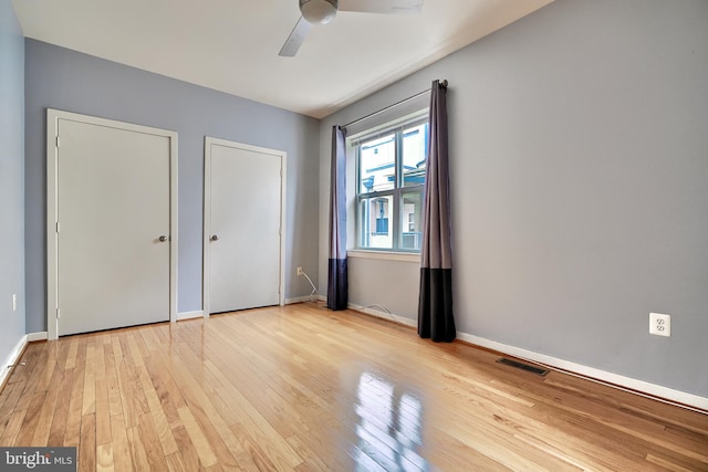 unfurnished bedroom featuring ceiling fan, light hardwood / wood-style floors, and two closets