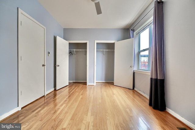 unfurnished bedroom featuring ceiling fan, two closets, and light wood-type flooring